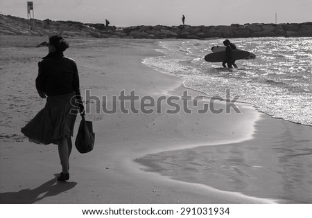 TEL AVIV, ISRAEL - MARCH 2, 2015: The silhouette of woman walking and surfers on the beach of Tel Aviv.