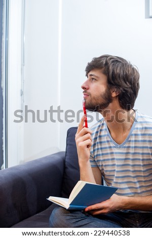 Caucasian student holding a blue notebook and thinking to himself.