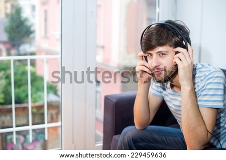 Student man listening to music on his headphones while sitting relaxed on the couch wearing a blue and white striped shirt.