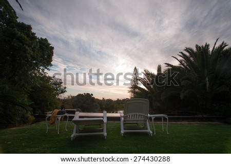 Pool with lawn-chairs during sunset.