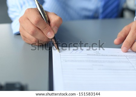 Businessman sitting at office desk signing a contract with shallow focus on signature