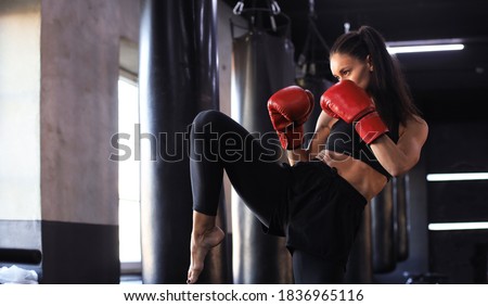 Kickboxing woman in activewear and red kickboxing gloves on black background performing a martial arts kick. Sport exercise, fitness workout.