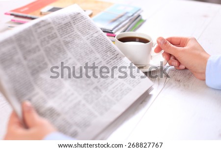 Close-up of female hand on cup of coffee during reading of newspaper