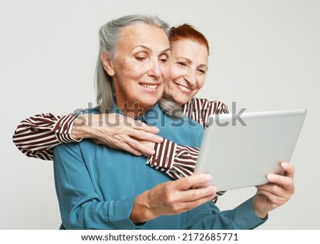 Two mature female friends looking through old photos digital album together with tablet device over grey background. Old friend Spending Quality Time Together. ストックフォト © 