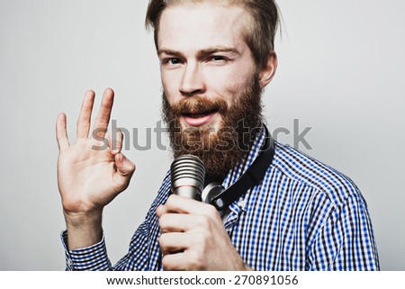 Life style concept: a young man with a beard wearing a white shirt holding a microphone and singing. Over gray background. Special Fashionable toning photos.