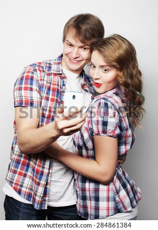 technology, love and friendship concept - smiling couple with smartphone, selfie and fun. Studio shot over white background.