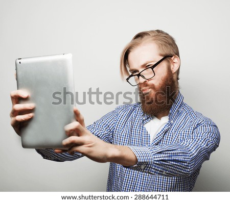life style, tehnology and people concept: Happy selfie. Young bearded man holding tablet and making photo of himself while standing against white background