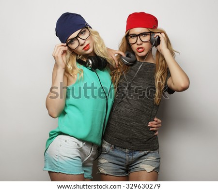 life style, happiness, emotional and people concept: Close up fashion lifestyle portrait of two young hipster girls best friends, wearing bright make up and similar trendy hats, making funny faces.