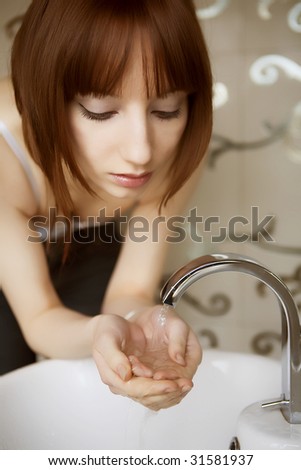 young woman washing her face in a basin and looking herself in the mirror
