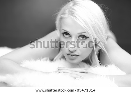 Black and white picture of a beautiful blonde model laying on a white fluffy fur.