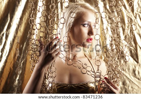 Beautiful blonde model in a gold swimsuit on a gold background with gold curtains around her.