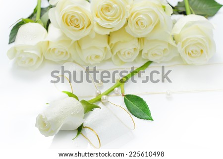 White rose flower with pearls and ribbon with a pile of roses in the background