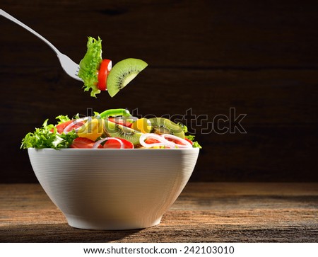 Fruit and vegetable salad in a bowl and picked by a fork on wooden background