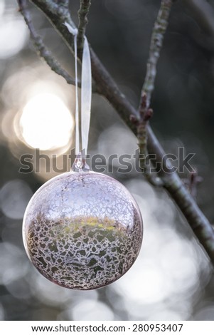 Christmas glass decoration hanging outside on the branch of a tree. Back lighting has caused a bokeh effect behind the bauble.