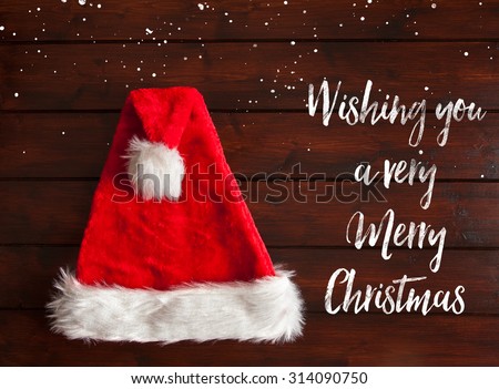 Red santa hat with white fur trim on brown wooden floorboards with snow drops effect. Text has a brushed effect.
