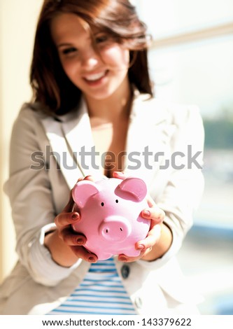 Young beautiful woman standing with piggy bank (money box), on building