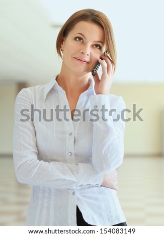 Portrait of young businesswoman talking on mobile phone on office hallway.
