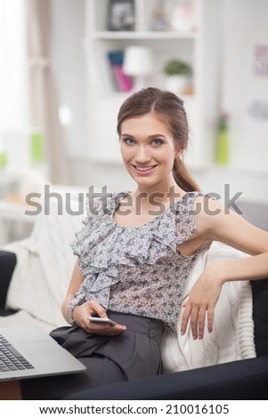 Young smiling beautiful woman sitting on the sofa with phone and laptop