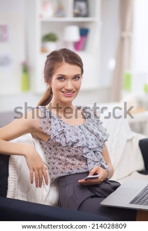 Young smiling beautiful woman sitting on the sofa with phone an