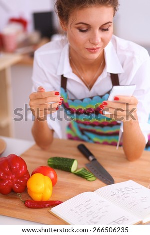 Smiling woman holding her cellphone in the kitchen