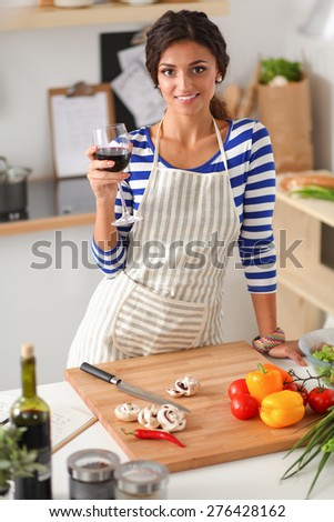 Young woman cutting vegetables in kitchen, holding a glass of wine