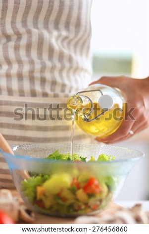 Smiling young woman  mixing fresh salad, holding bottle of oil