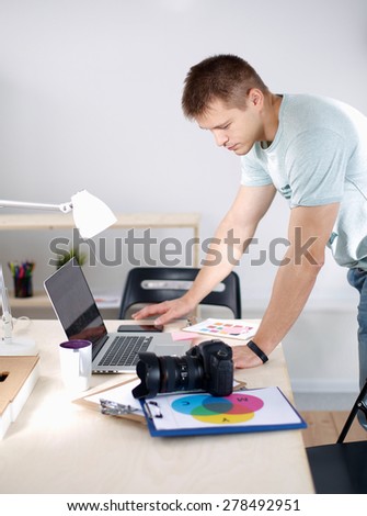 Male photographer standing near  the desk with laptop
