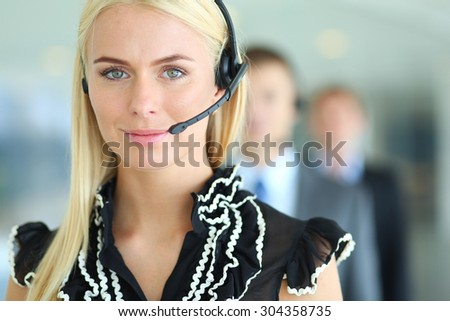 Businesswoman with headset smiling at camera in call center. Businessmen in headsets on background