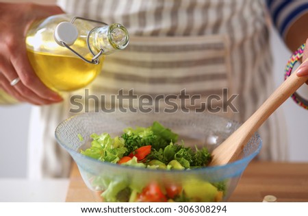 Young woman mixing fresh salad, standing near desk
