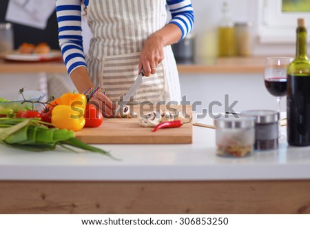 Young woman cutting vegetables in kitchen, standing near desk