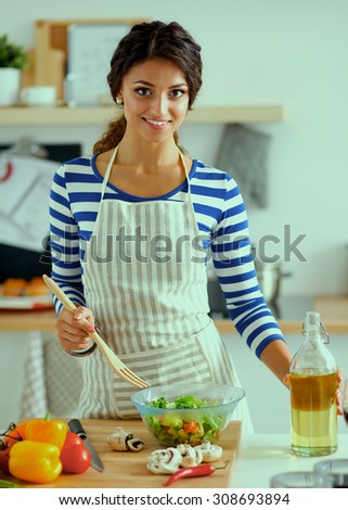 Young woman mixing fresh salad, standing near desk