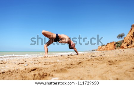 Young man doing yoga pose at the deserted sea beach