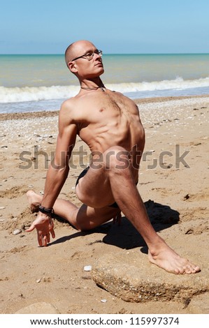 Yoga practice. Muscular man in King Pigeon Yoga Pose at the beach