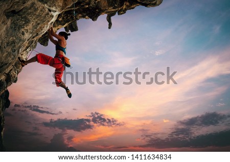 Athletic Woman climbing on overhanging cliff rock with sunset sky background Сток-фото © 