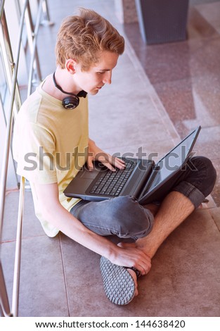 Teenage boy using internet sitting in commercial center floor