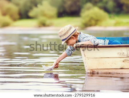 Little boy launch paper ship from old boat on the lake