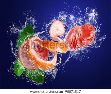 Red grapefruit with peeled skin  and leaves in water drops on the dark blue background