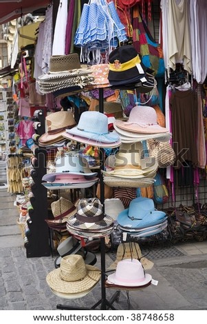 Hats on a rack on the sidewalk of a store.