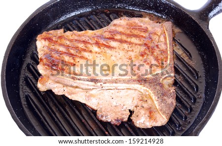 Close up of a big sirloin and rump beef steak with t-bone sizzling in a hot pan. Image isolated on white studio background.