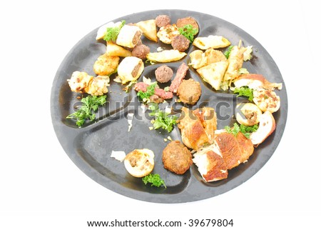 A big black plate with various food (left overs) after a party. Image isolated on white studio background.