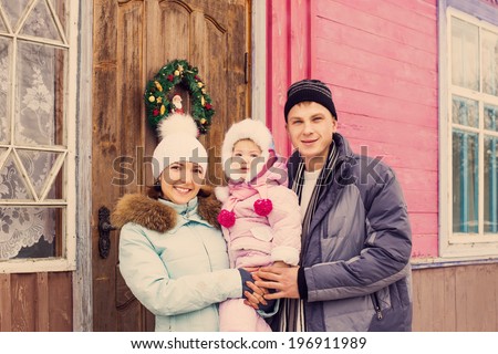 Beautiful family in warm clothes standing  of his house in winter