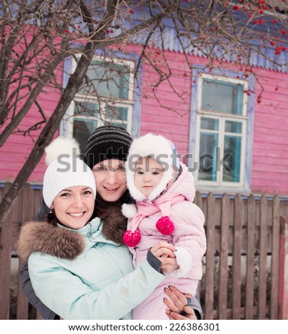 Beautiful family in warm clothes standing of his house in winter