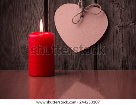 red candle and paper heart on wooden background