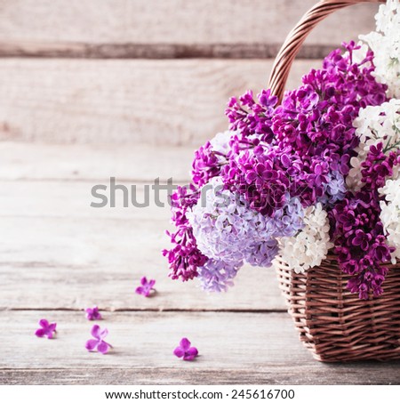 basket with a branch of lilac flower on a wooden background