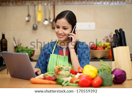 Young woman using a tablet computer in her kitchen and taking on cellphone