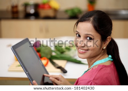 Cheerful Indian woman using a tablet computer in her kitchen