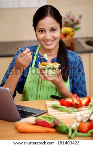 Young Indian woman with kitchen apron and eating salad