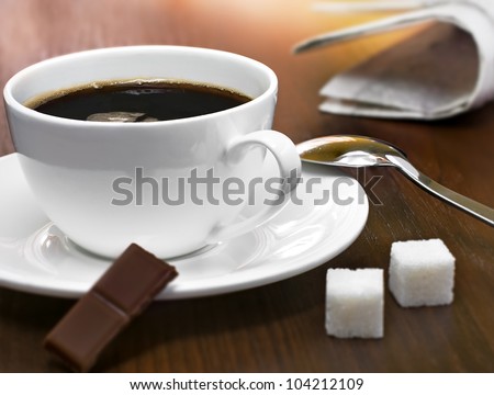 Coffee cup, sugar cubes, chocolate and newspapers on a table, studio shot