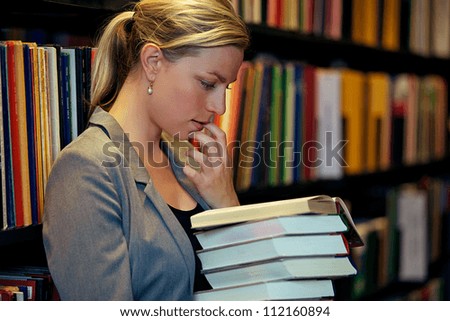 Beautiful female student standing in a library deeply immersed in a book wth her finger to her lip in thought