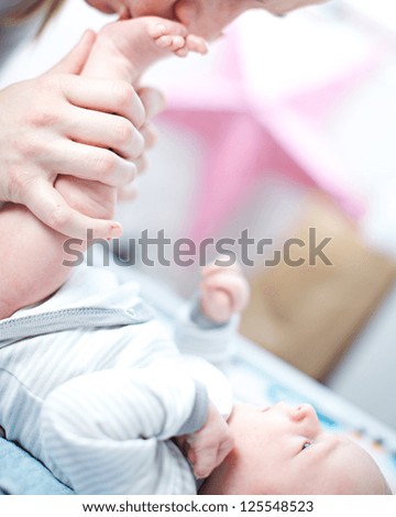 Closeup cropped portrait of a young mother kissing the feet of her baby as it lies on its back in the nursery